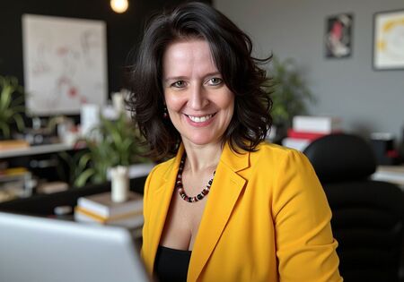 Nicole Angela Buck – KI-Trainerin und Kommunikationsdesignerin in ihrem Atelier, lächelnd in gelbem Blazer